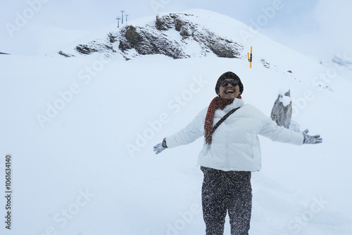 An asian man in warm clothing and sunglasses standing on snowcapped mountain photo