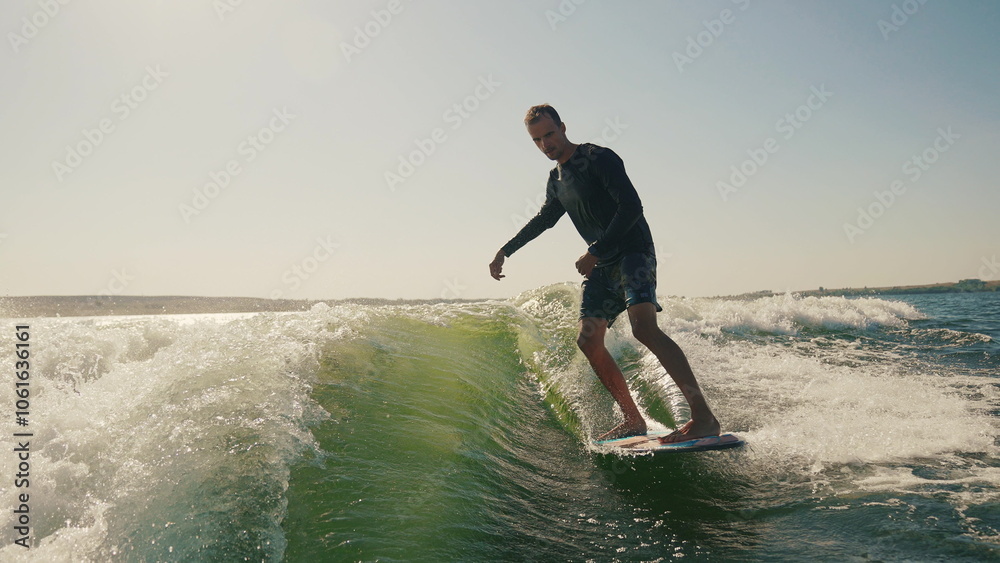 Wakeboarding behind a motor boat on the water surface. An athlete performs tricks while balancing on a board. The scene conveys the dynamics, speed and adrenaline of water extreme sports Wakeboarding behind a motor boat on the water surface. An athlete performs tricks while balancing on a board. The scene conveys the dynamics, speed and adrenaline of water extreme sports
