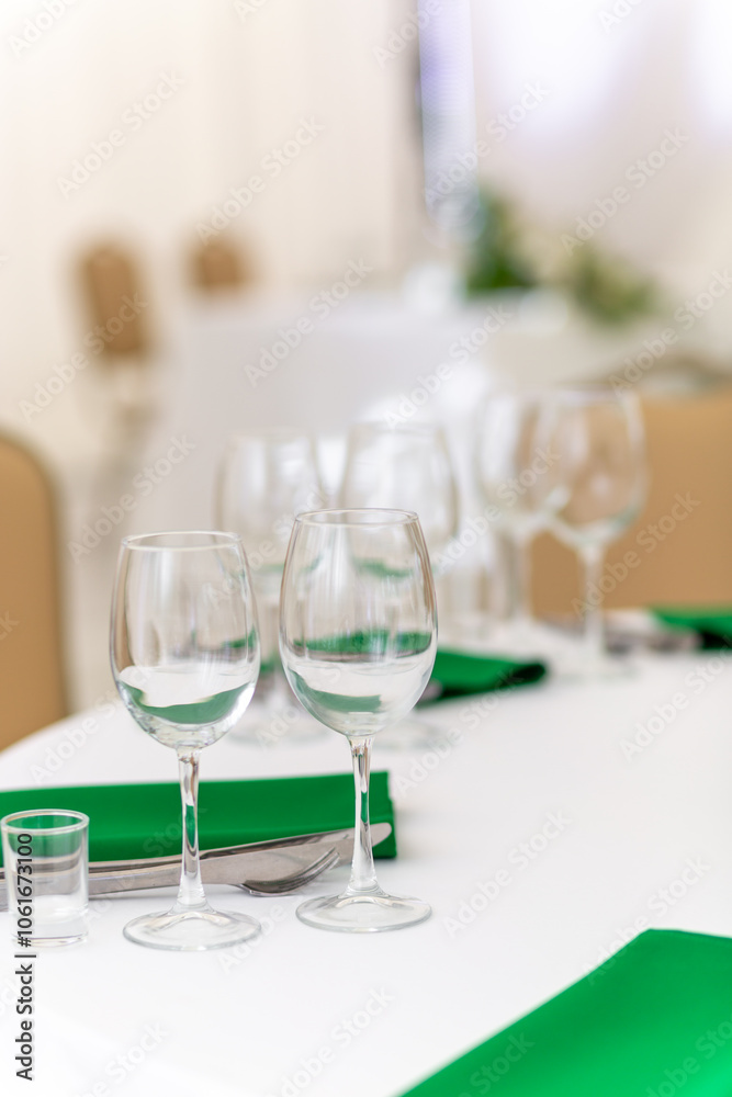 Close up of wine glasses, silver tableware and green napkins on round tables covered with white tablecloth. Close up of wine glasses, silver tableware and green napkins on round tables covered with white tablecloth.
