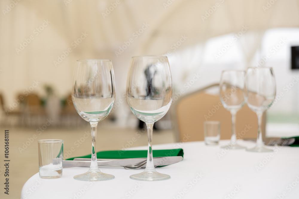 Close up of wine glasses, silver tableware and green napkins on round tables covered with white tablecloth. Close up of wine glasses, silver tableware and green napkins on round tables covered with white tablecloth.