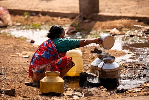 Woman collecting water from puddle, India