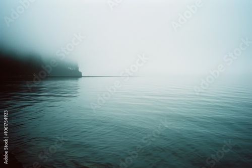 Fog envelops a quiet lakeside, blurring the horizon and instilling a sense of calm and mystery in the tranquil scene. photo