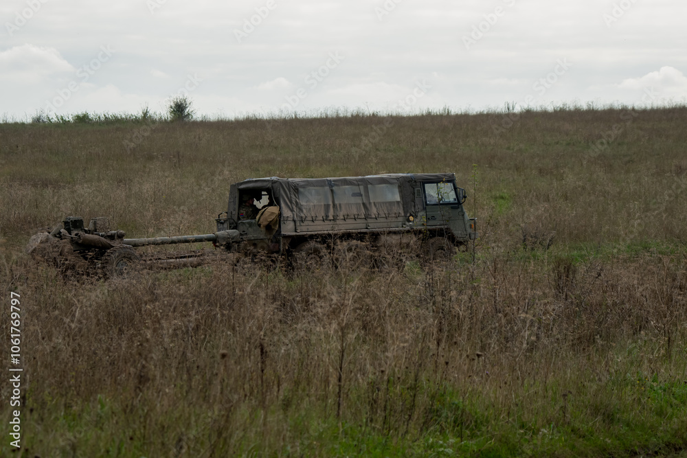 Fototapeta premium British army bae systems, Puch, Daimler, Pinzgauer High-Mobility All-Terrain 6x6 vehicle towing a 105mm Light Artillery Gun on a military exercise