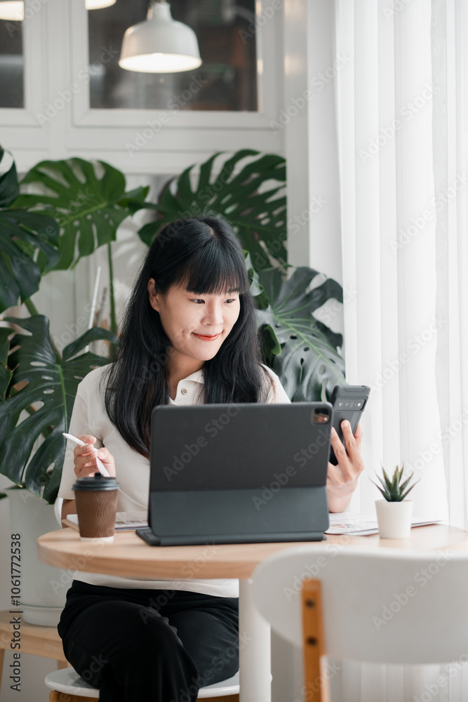 A young woman multitasks using a laptop and smartphone in a bright, plant-filled home office setting. A young woman multitasks using a laptop and smartphone in a bright, plant-filled home office setting.