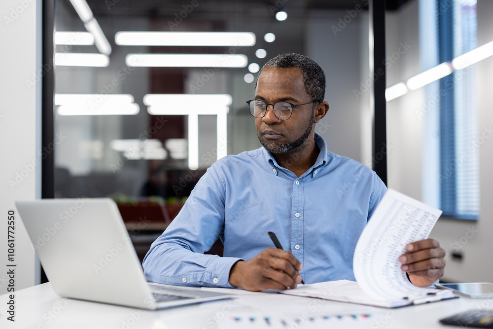 Mature African American businessman in modern office working on laptop, reviewing documents. Focused, professional, productive atmosphere, emphasizing business analysis, decision-making, and strategy Mature African American businessman in modern office working on laptop, reviewing documents. Focused, professional, productive atmosphere, emphasizing business analysis, decision-making, and strategy