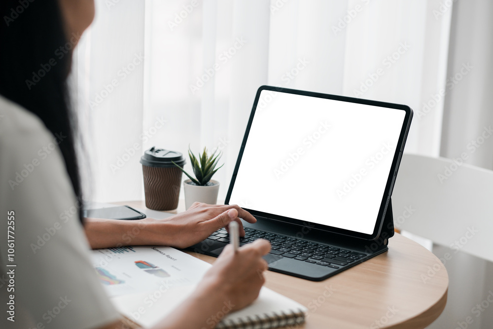 A woman using a tablet with a blank screen at a home office desk, accompanied by a coffee cup and notebook. A woman using a tablet with a blank screen at a home office desk, accompanied by a coffee cup and notebook.