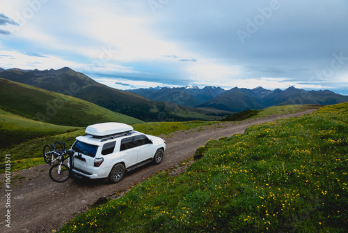 Offroad car carrying bikes on flowering grassland mountain under blue sky