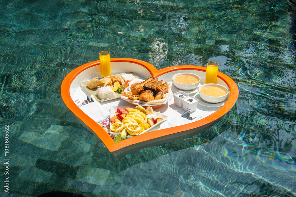 Floating heart-shaped plate with a breakfast of fruits, rice, fish, buns, juice in the swimming pool in the Maldives