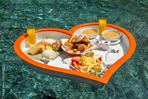 Floating heart-shaped plate with a breakfast of fruits, rice, fish, buns, juice  in the swimming pool in the Maldives