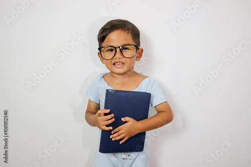 Portrait Of Little Asian Schoolboy In Eyeglasses Reading Book While Standing Isolated Over Blue Studio Background, Nerdy Preteen Korean Male Kid Enjoying Study And Learning Process, Copy Space