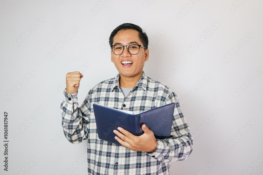Adult Asian man showing excited gesture with fist clenched when reading a book. Adult Asian man showing excited gesture with fist clenched when reading a book.