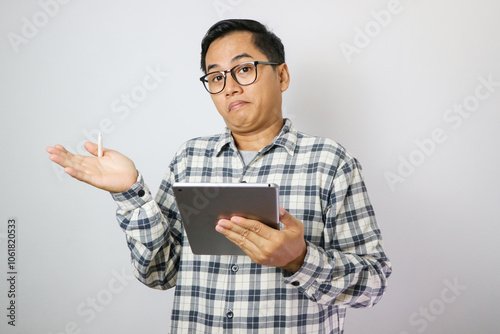 Adult Asian man holding mobile tablet device with confused face expression