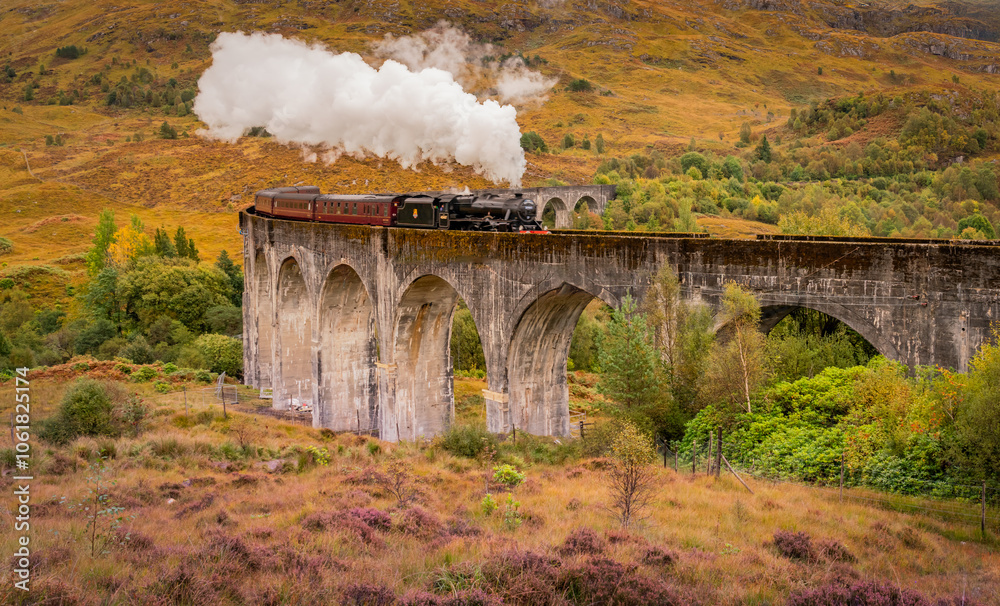 Fototapeta premium Steam train at Glenfinnan Autumn in Scotland with reflections in the lochs