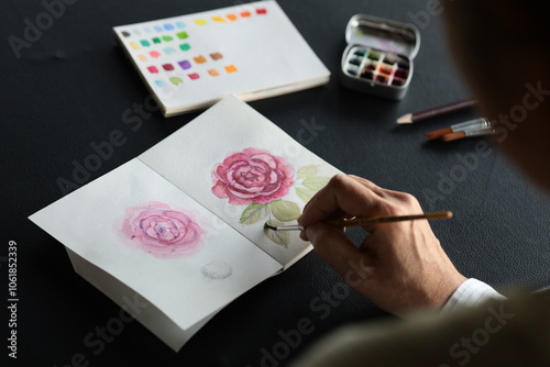 A hand painting beautiful roses on watercolor paper, surrounded by paint palettes and brushes, capturing the creative process."