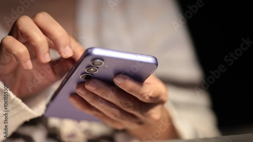 Hands holding a smartphone in a focused manner, likely browsing or reading, with a close-up view and blurred background for depth