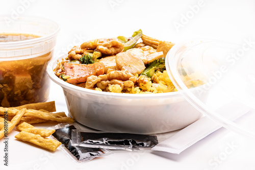 Chinese restaurant takeout lunch special: Szechuan chicken with vegetables, hot and sour soup, Asian crackers, soy sauce packets, and chopsticks, all packed in disposable plastic containers. photo