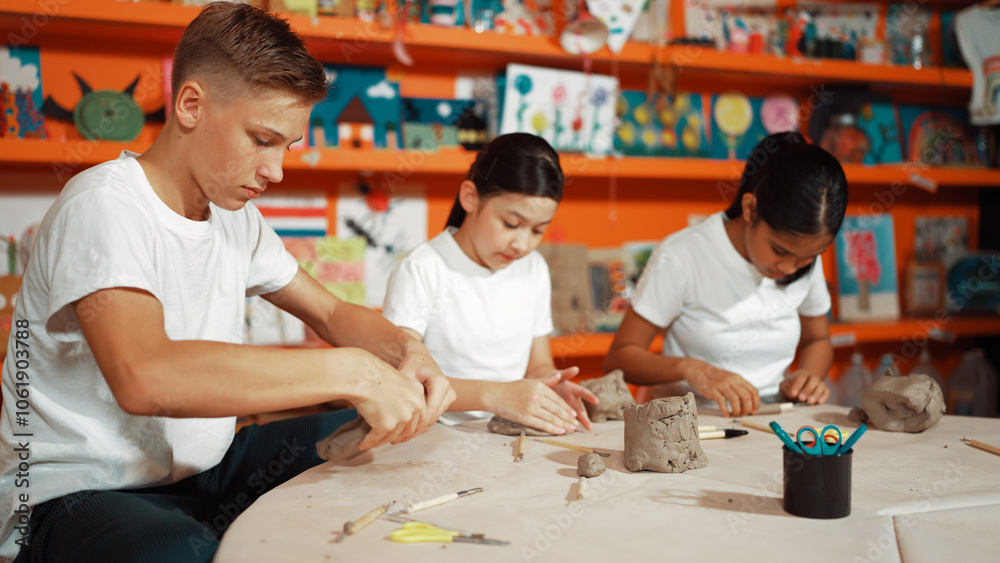 Caucasian smart teenager modeling clay while craving glass of clay at art lesson. Group of multicultural happy student working at dough in pottery workshop. Creative activity concept. Edification. Caucasian smart teenager modeling clay while craving glass of clay at art lesson. Group of multicultural happy student working at dough in pottery workshop. Creative activity concept. Edification.