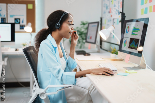 Young woman working with headset and computer analyzing graphs, charts and reports in modern office