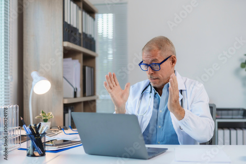 Senior male doctor gesturing and having video conference on laptop in medical office