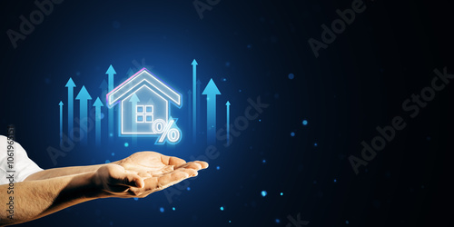 Hands holding a glowing house icon with a percent sign and upward arrows on a dark blue background. Mortgage concept.