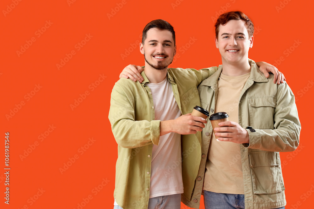 Male friends with coffee cups hugging on orange background Male friends with coffee cups hugging on orange background