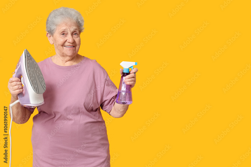 Happy senior woman with iron and spray bottle of water on yellow background Happy senior woman with iron and spray bottle of water on yellow background