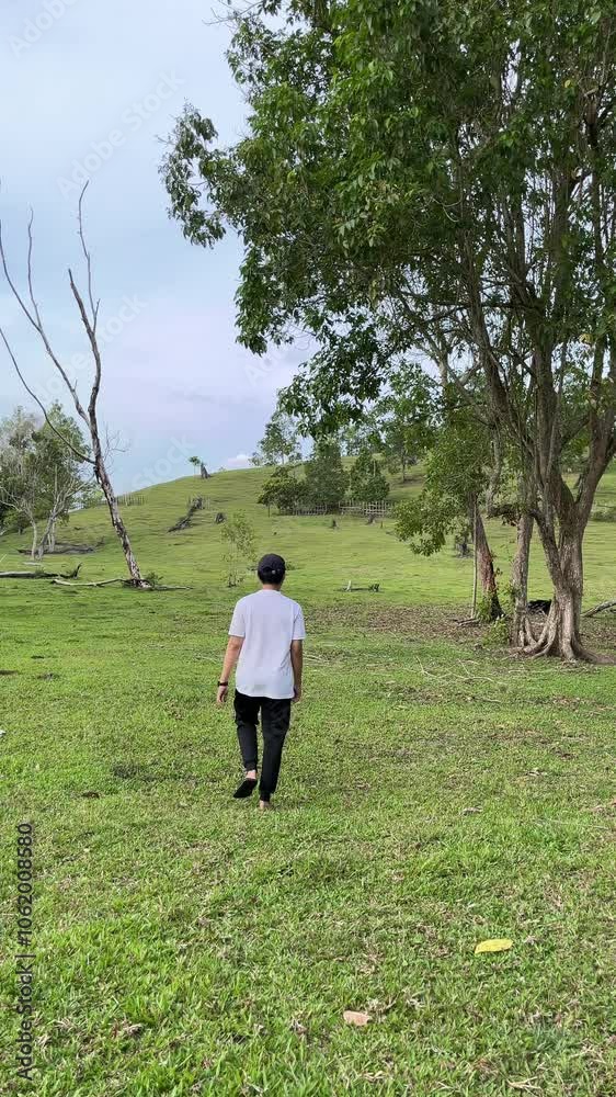 back view an asian man is walking or running forward in a meadow shot from behind. back view an asian man is walking or running forward in a meadow shot from behind.