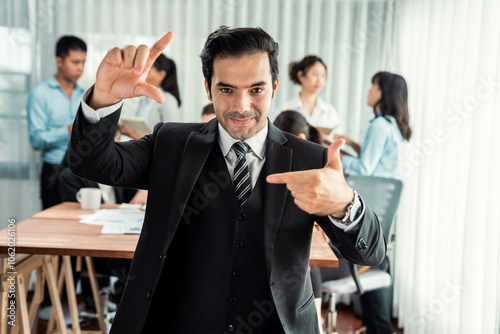 Portrait of happy businessman looking at camera, making hand holding gesture for advertising product with motion blur background of business people movement in dynamic business meeting. Habiliment