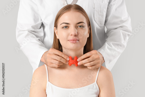 Male endocrinologist with thyroid gland model and young woman on grey background, closeup photo