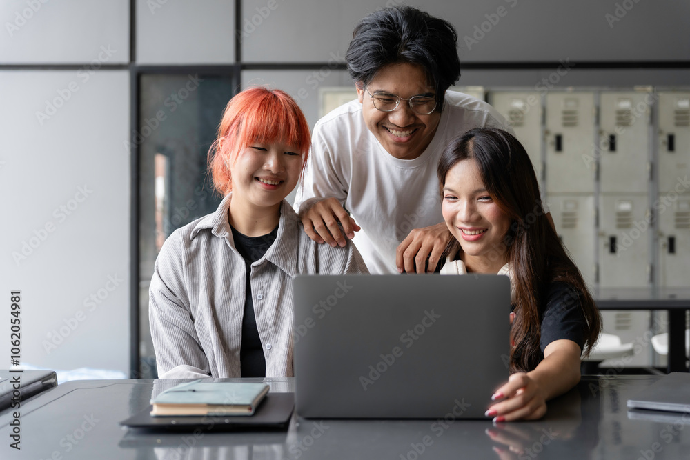 Three cheerful young asian colleagues working together, using laptop, enjoying teamwork and cooperation in modern office Three cheerful young asian colleagues working together, using laptop, enjoying teamwork and cooperation in modern office
