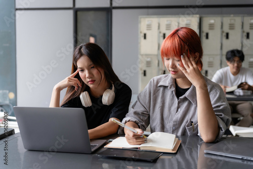 Two young asian female students are feeling tired and stressed while studying together in a library