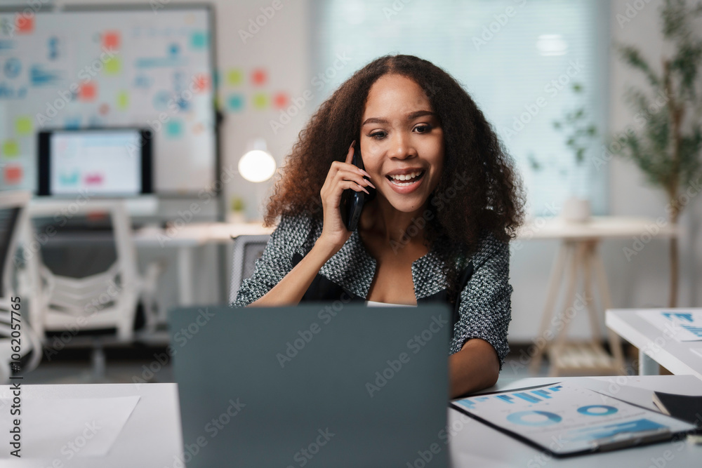 Obraz premium Smiling businesswoman making a phone call and looking at laptop while working on a project in modern office