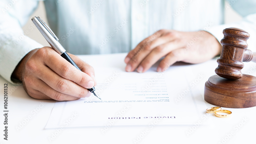 Human hand signing divorce contract, close-up. Wedding rings with marriage contract and judge gavel on a background Human hand signing divorce contract, close-up. Wedding rings with marriage contract and judge gavel on a background