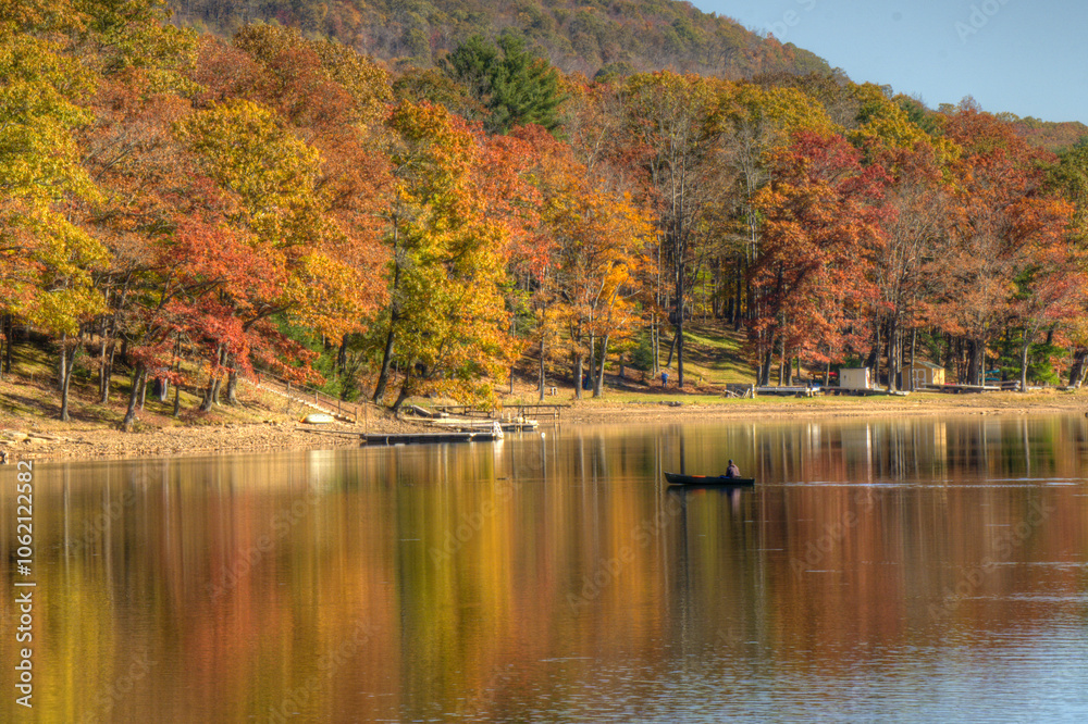 A serene lake scene captures vivid autumn colors as the trees reflect on the calm water. A lone boat drifts gently, enhancing the tranquil atmosphere. A serene lake scene captures vivid autumn colors as the trees reflect on the calm water. A lone boat drifts gently, enhancing the tranquil atmosphere.