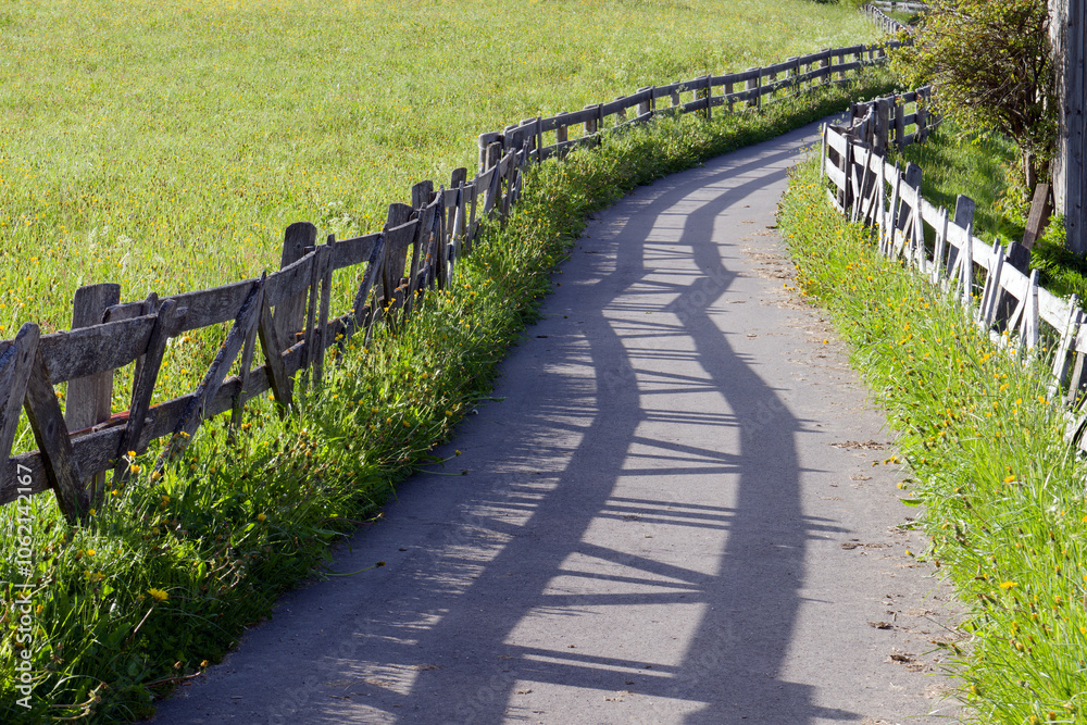 Wooden fence along meadows and a road with interesting shadow, Alps, Europe Wooden fence along meadows and a road with interesting shadow, Alps, Europe