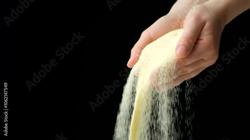 Hands pouring dry semolina durum flour, black background, copy space for text, slow motion