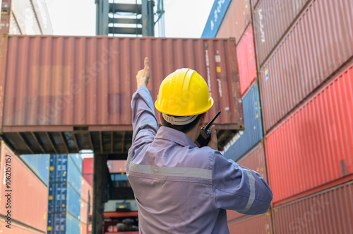 Obraz na plátne Loading foreman in yellow helmet directing crane operator to lift shipping container at shipyard