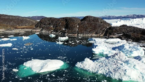 Explore the breathtaking beauty of Greenland's glacial environment where shimmering waters reflect majestic mountains surrounded by ice formations during summer.