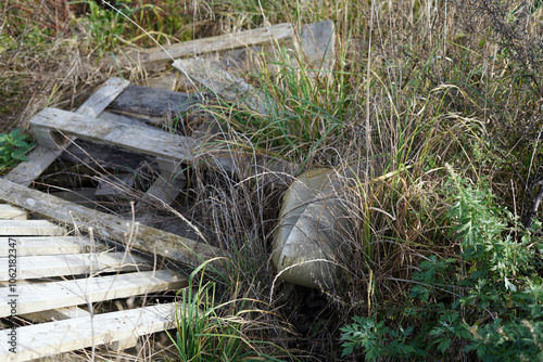 Overgrown mess in the grass. We see damaged wooden pallets and other waste.