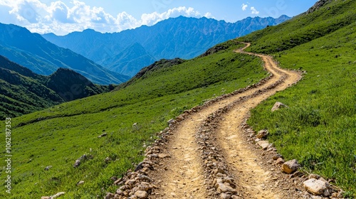 A winding dirt road leads up a grassy hillside towards a majestic mountain range. The sky is blue with fluffy white clouds.