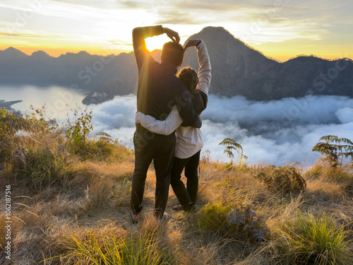 Rear view of a Couple making a heart sign while watching the sunset on a climbing trip, Mount Rinjani, Lombok, West Nusa Tenggara, Indonesia photo