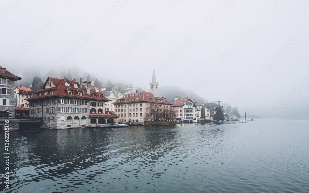 Fototapeta premium A foggy morning view of a lakeside town with traditional architecture.