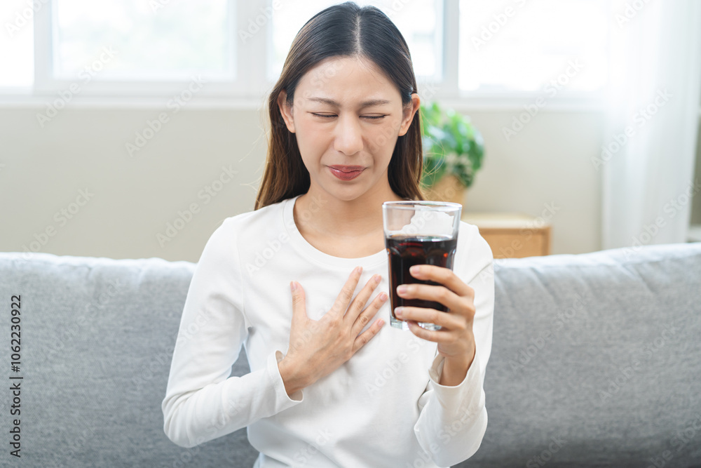 Acid reflux disease, suffer asian young woman, girl hand holding a glass of cola, have symptom gastroesophageal, heartburn pain on chest when drinking sparkling, soft water. Healthcare medical concept Acid reflux disease, suffer asian young woman, girl hand holding a glass of cola, have symptom gastroesophageal, heartburn pain on chest when drinking sparkling, soft water. Healthcare medical concept