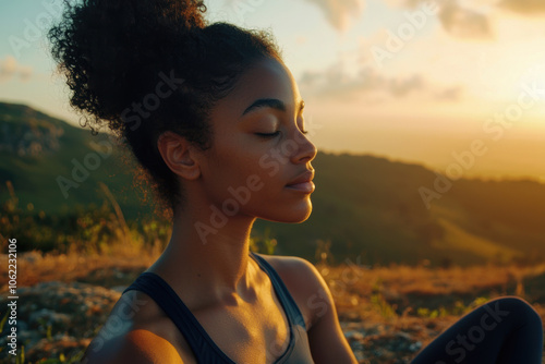 A woman meditating outdoors on a mountain top, surrounded by nature, wearing simple yoga attire, gentle wind blowing, distant sunrise casting warm light, calm and serene facial expression, close-up