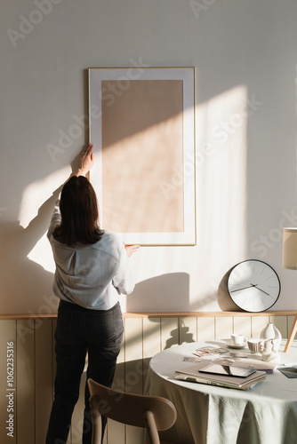 Rear view of a woman hanging a blank picture frame on a  wall in a living room photo