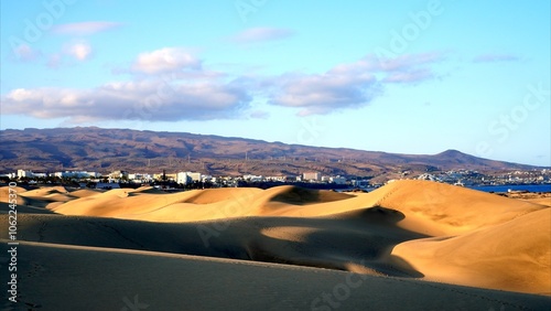 Maspalomas sand dunes with Playa San Agustin tourist resort and rocky mountains in the background. Textures on golden sand and curves in shadow at sunset