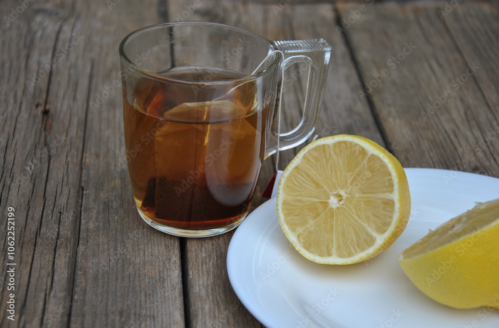 On a wooden table a glass mug with tea and lemon on a plate. selective focus. tea with lemon On a wooden table a glass mug with tea and lemon on a plate. selective focus. tea with lemon