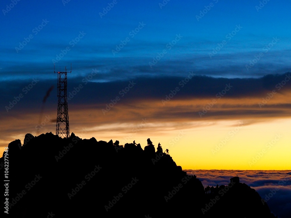 A tall communication antenna tower stands silhouetted against a vibrant, colorful sunset sky, capturing the essence of modern connectivity and natural beauty - Pico do Arieiro, Madeira, Portugal. A tall communication antenna tower stands silhouetted against a vibrant, colorful sunset sky, capturing the essence of modern connectivity and natural beauty - Pico do Arieiro, Madeira, Portugal.