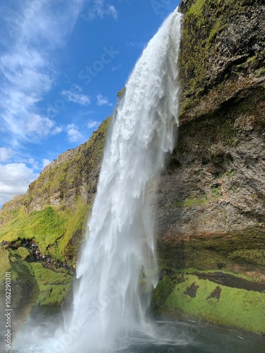 Seljalandsfoss waterfall in Iceland, cascading dramatically over a cliff. The powerful stream of water flows gracefully, framed by lush greenery and a stunning backdrop of rugged landscapes.