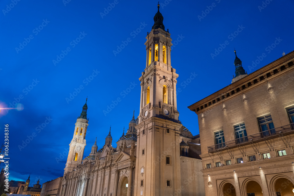 Illuminated Basilica del Pilar in Zaragoza, Spain, at dusk, with serene reflections on the Ebro River. Ideal for travel, architecture, and cultural themes. Illuminated Basilica del Pilar in Zaragoza, Spain, at dusk, with serene reflections on the Ebro River. Ideal for travel, architecture, and cultural themes.